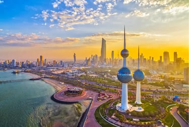 Aerial view of Kuwait Towers and Kuwait City skyline at golden hour sunset along the Persian Gulf coast.