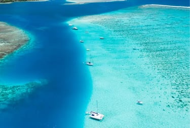 Aerial view of sailboats anchored in a crystal clear turquoise lagoon with tropical coral reefs.