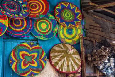 Handwoven Ethiopian colorful wicker baskets and traditional flat plates hanging on a blue wall.