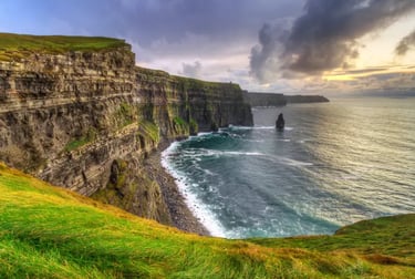 Panoramic view of the Cliffs of Moher in Ireland at sunset with green grass and crashing waves.