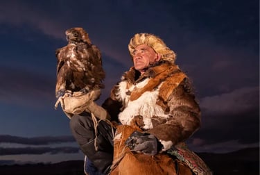 A Mongolian golden eagle hunter in traditional fur clothing posing with his bird at dusk.