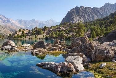 Crystal clear blue mountain lake with jagged rocks and pine trees in the Fann Mountains of Tajikistan.