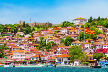 Panoramic view of Ohrid's old town waterfront featuring red-roofed houses and Samuel's Fortress in North Macedonia.