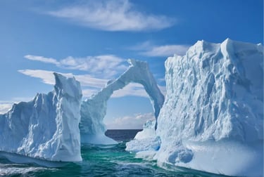 Large blue icebergs and a natural ice arch floating in the Antarctic ocean under a bright sunny sky.