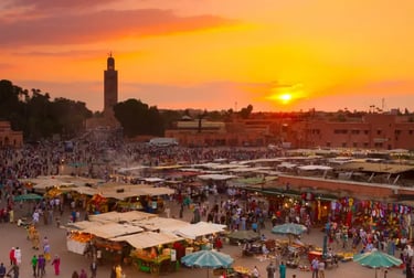A crowded Jemaa el-Fnaa market square in Marrakech at sunset with the Koutoubia Mosque in the background.