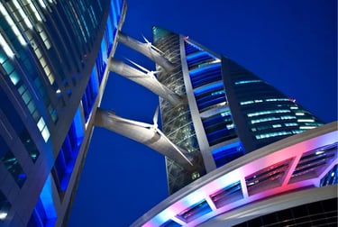 Low-angle view of the Bahrain World Trade Center towers and wind turbines illuminated at night.