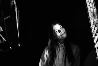 Black and white portrait of a smiling woman holding a mug in a professional studio setting with lighting equipment.
