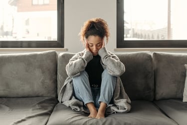 Stressed woman sitting on a couch holding her head, symbolizing mental health and anxiety.