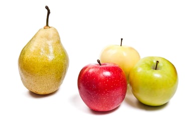 A fresh yellow pear standing next to three organic red and green apples on a white background.