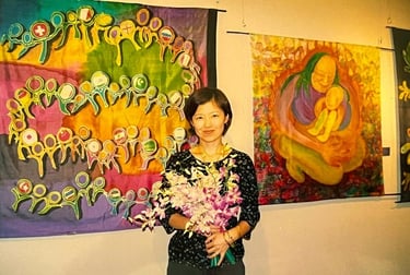 Kayoko standing with a bunch of flowers with two of her textile exhibits in the background.