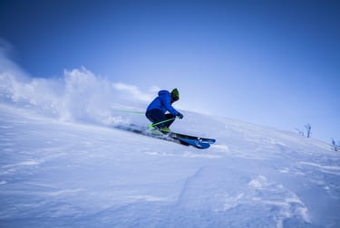 Un esquiador con chaqueta azul se abre paso entre la nieve polvo en una empinada ladera de montaña 