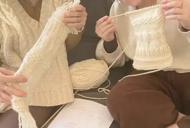 Two women holding up their cream beginner knitting projects at The Paddock and Purl Studio.