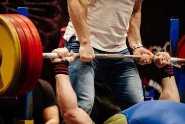 A spotter assists a powerlifter during a heavy bench press with a weighted barbell.
