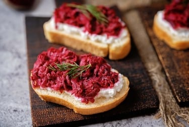 Beetroot and goat cheese crostini appetizer garnished with fresh dill on a rustic wooden board.