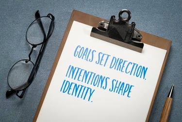 Motivational quote about goals and intentions on a clipboard with glasses and a pen.