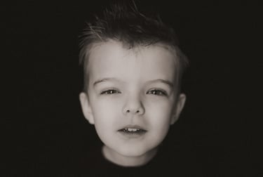 4-year-old boy squints curiously into the camera during a personality portrait session on a black ba