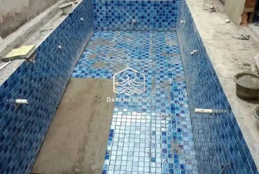 Proses pemasangan material finishing mozaik pada dinding kolam renang oleh tukang berpengalaman.