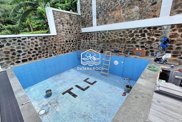 Proses pemasangan material finishing mozaik pada dinding kolam renang oleh tukang berpengalaman.