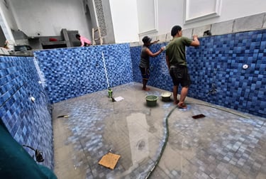 Proses pemasangan material finishing mozaik pada dinding kolam renang oleh tukang berpengalaman.