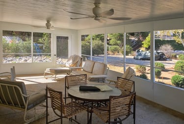 Backyard woth shrubs and rocks viewed from inside a white screen room.