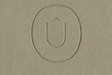 Logotipo minimalista en relieve que presenta una U con un circunflejo dentro de un óvalo.