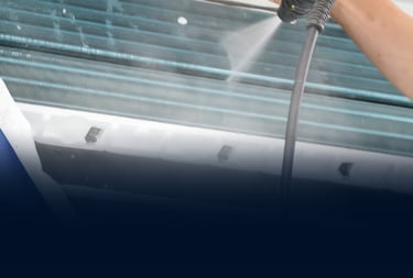 Professional technician cleaning air conditioner evaporator coils with a high-pressure water spray tool.