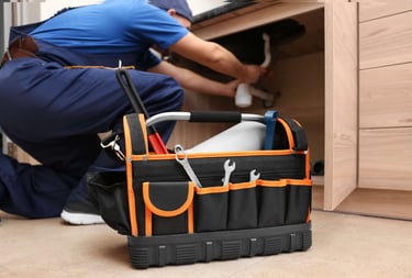 Professional plumber with tool box repairing leaking kitchen sink drain.
