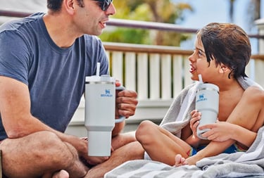 Adulto e criança usando garrafas Stanley em ambiente externo, destacando momentos em família e prati