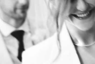 A blurred black and white close-up of a smiling bride and groom in wedding attire.