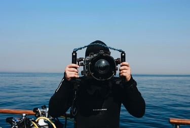 A scuba diver in a black wetsuit holding a professional underwater camera housing on a boat.