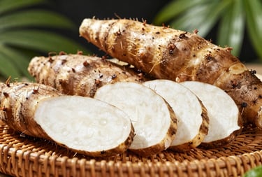 Fresh malanga roots with their characteristic brown skin and white interior, arranged neatly on a woven tray in a tropical sunlight environment.