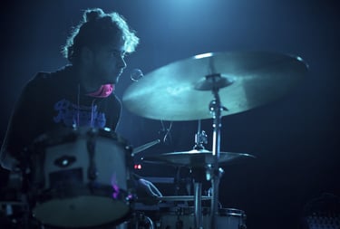 A male drummer performing a live concert on a drum kit under blue stage lighting.
