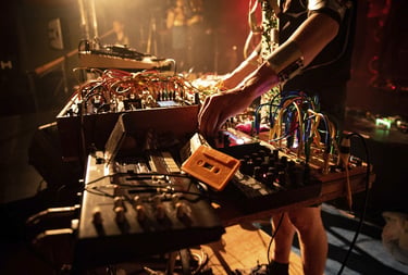 Electronic music artist performing live with a modular synthesizer, patch cables, and analog gear.