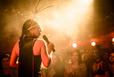 A singer in an avant-garde headpiece performs live on a smoky stage for a crowd.