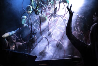 Performers interact with a surreal, smoky wire sculpture during a dark experimental theater production.