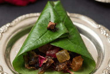 Traditional Indian sweet meetha paan folded in a betel leaf with gulkand and spices on a silver plate.