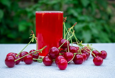A glass of fresh red cherry juice surrounded by ripe cherries on a table outdoors.