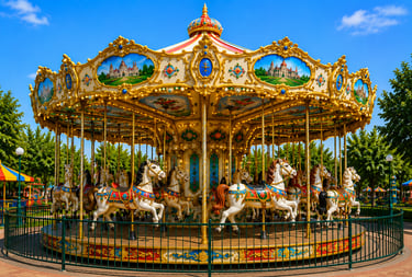 A colorful vintage carousel with ornate white horses at an outdoor amusement park under a blue sky.