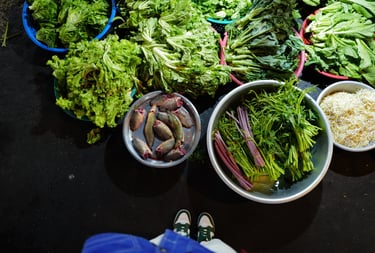Overhead view of baskets of fresh greens and fish on a market floor, By ACAT Photos.