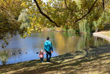 Bild von einer erwachsenen Person, die mit einem Kind an der Hand an einem See spazierengeht.