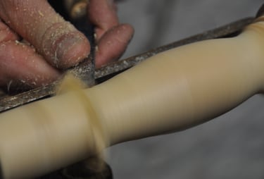 A close-up of a hand holding a chisel, turning wood spinning on a lathe