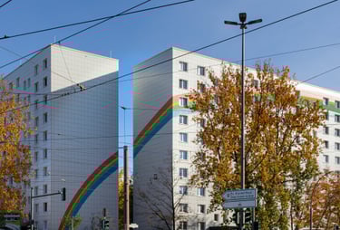Bild von zwei nebeneinanderstehenden weißen Hochhäusern mit aufgemaltem Regenbogen.
