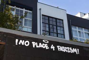 Bild von schwarzen und weißen Häusern, im Vordergrund ist das Graffitti "No room for facism".