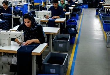 Workers at a production facility using industrial sewing machines to assemble garments.