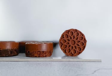 Miniature round brownie cakes with intricate geometric floral designs on a white surface.