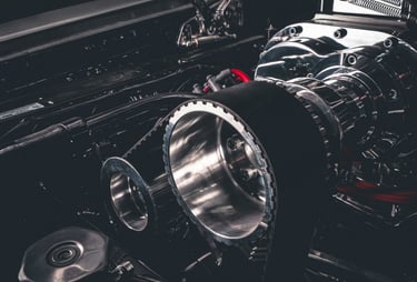 Close-up of a high-performance chrome supercharger engine with a black drive belt and pulleys.