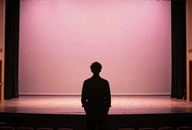 A silhouette of a lighting designer looking at an empty theater stage in North America, with a soft pink glow from the wings.