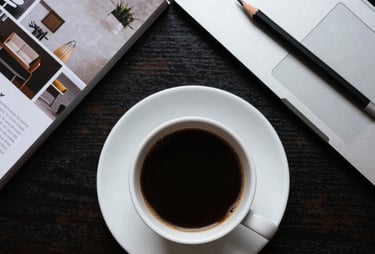 A top-down view of a designer's desk with a cup of coffee, architectural magazines, and a professional digital drafting pencil.