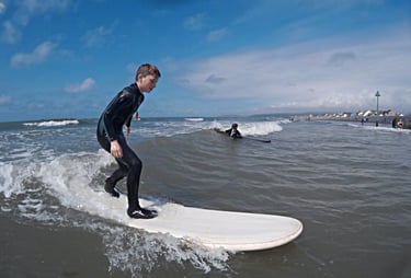 A young male surfing standing up riding a wave with sunshine and blue skies