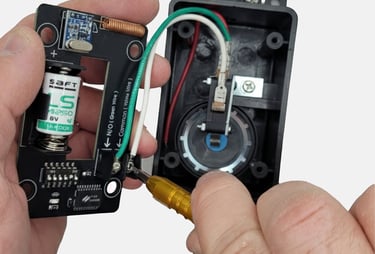 Technician using a screwdriver to repair a wireless transmitter circuit board with a lithium battery.